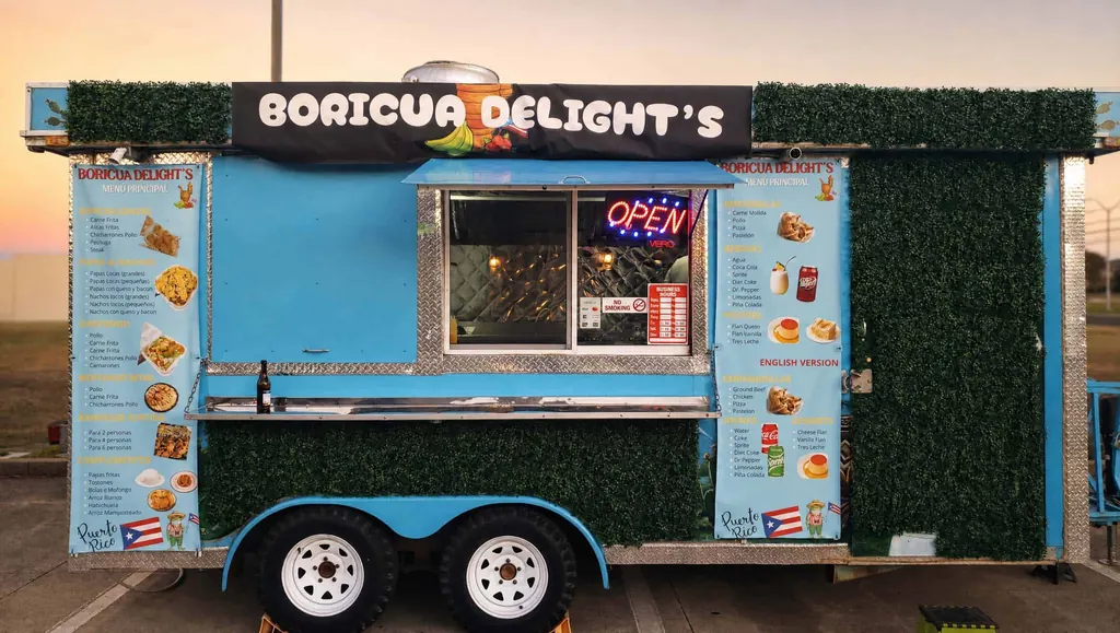 The blue Boricua Delight food truck at sunset with its menu boards and open sign lit